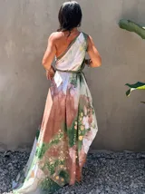 Vestido largo de tela fluida, color verde esmeralda con estampado abstracto en tonos turquesa y detalles dorados. Diseño asimétrico con un solo tirante tejido en el hombro.