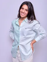 Camisa blanca de algodón, corte holgado, con cuello clásico y botones frontales. Las mangas son largas y se ven remangadas.