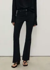 Pantalón de jean negro de tiro medio, corte ajustado hasta la rodilla y acampanado en la parte inferior, con bajo deshilachado.