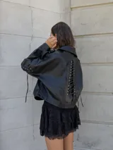 Campera negra de cuero sintético, estilo biker, con cierre cruzado y detalles de hebillas en los hombros.