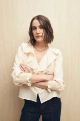 Camisa blanca a rayas verticales, con escote en V, mangas 3/4 con puños elastizados y volados.