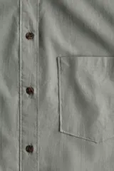 Camisa verde claro de lino y algodón, corte amplio, con cuello clásico, cierre frontal con botones, bolsillo de parche en el pecho, mangas largas con puños abotonados y bajo redondeado con aberturas laterales.