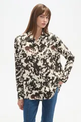 Camisa holgada de manga larga, color negro, con cuello camisa y botones frontales. Presenta apliques de tachas plateadas en los hombros y a lo largo de la tapeta frontal.