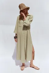 Vestido camisero largo color verde claro, confeccionado en lino. Tiene cuello solapa, escote en V, manga tres cuartos con trabilla y botón, bolsillos delanteros de plastrón, aberturas laterales en el ruedo y cierre frontal con botones.