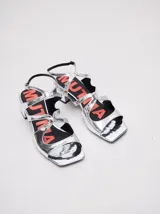 Sandalias de cuero charol color borgoña con tiras finas, taco cuadrado bajo y cierre con hebilla en el tobillo. Interior con estampado del logo de la marca en color naranja.