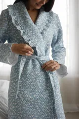 Bata larga celeste con estampado de pajaritos blancos, confeccionada en algodón capitoneado con volados en la solapa y puños. Incluye lazo de algodón capitoneado para ajustar en la cintura.