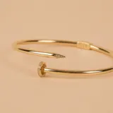 Brazalete rígido abierto de oro amarillo 18k con forma de clavo y detalles de circonias.