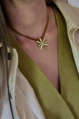 Collar con cordón marrón y dije dorado en forma de estrella de ocho puntas.