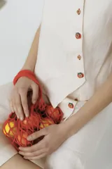 Top sin mangas de lino color crudo, con cartera asimétrica y botones de madera. Tiene ojales bordados con forma de frutillas.