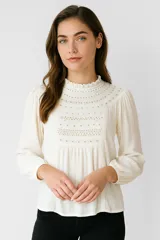 Blusa color crema de viscosa con bordados, mostacillas y encaje. Tiene cuello a la base, mangas largas abullonadas y corte al cuerpo.