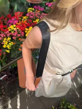 Bandolera pequeña de textura símil cuero color caramelo/marrón, con dos compartimentos principales con cierre. Correa ancha ajustable de tela negra con inscripción en relieve.