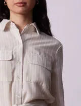 Vestido camisero corto a rayas verticales color beige, con cuello con solapa, abertura central con botones, bolsillos aplicados en el pecho y lazo de ajuste en la cintura.