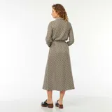 Vestido camisero largo con estampado geométrico en tonos beige, negro y blanco. Tiene cuello camisero, mangas largas con puños abotonados, cierre frontal con botones y cinturón de lazo.