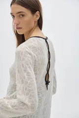 Túnica tipo vestido tejido calado color blanco, con cuello en V y ribete negro, abotonada adelante, de largo midi y con cortes a los lados.