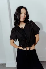 Blusa negra con bordado calado, escote en V con lazos para atar y mangas cortas abullonadas.