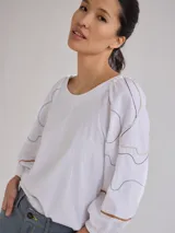 Remera gris de algodón con mangas color beige con bordados de líneas en blanco, amarillo y gris.