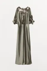 Vestido midi color verde oliva de tejido satinado, con cuello barco, mangas cortas abullonadas con puños y aplicación de encaje a contraste en la parte superior. Cierre trasero con cremallera oculta y botones forrados.