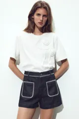 Camiseta blanca de cuello redondo y manga corta con detalle de flores con volumen en delantero a tono.