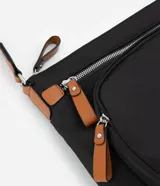 Bandolera negra de poliéster con detalles en cuero sintético color marrón. Tiene correa transversal ajustable, cierre de cremallera, bolsillos delanteros y placa metálica con el logo de la marca.