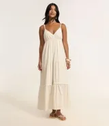 Vestido largo midi color crudo, con escote en V, breteles finos con detalles trenzados, lazo en la espalda, volados y adornos en el bajo.