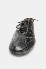 Zapato plano de cuero negro con efecto desgastado y cordones.
