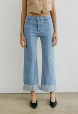 Pantalón de jean azul oscuro con corte acampanado, tiro medio y dobladillo en el ruedo. Presenta costuras marcadas en el frente y estampado abstracto en tonos grises y blancos en el interior del dobladillo.