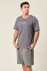 Bermuda deportiva gris de nylon, de corte suelto, con cintura elástica y cordón de ajuste. Cuenta con detalles de líneas negras en los costados y bolsillos con cierre.