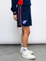 Short deportivo azul marino con ribetes blancos y rojos, y escudo del Club Nacional de Football bordado en la pierna derecha.