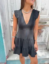 Vestido corto negro con escote en V profundo, detalles de encaje bordado en el busto y volados en el ruedo.