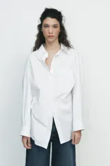 Camisa negra de cuello solapa y manga larga amplia. Tiene un bolsillo de parche en el delantero, detalle de pliegues y cierre frontal con botones.