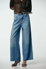 Pantalón de jean celeste de tiro alto, corte wide leg cropped, con cinco bolsillos y cinturón marrón con tachas.