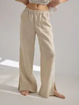 Pantalón de lino color beige, de corte clásico y pierna recta con tajos laterales en el ruedo. La cintura es elastizada.
