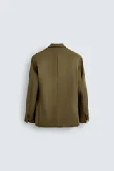 Blazer color verde oliva de corte regular, confeccionada en tejido con lana. Presenta cuello con solapas de pico, manga larga con puños abotonados, bolsillo de vivo en pecho, bolsillos de doble vivo en cadera, bolsillo interior y aberturas en la espalda. Cierre frontal cruzado con doble botonadura.