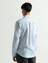 Camisa celeste y blanca a rayas verticales, de manga larga y corte clásico. Tiene cuello abotonado y bolsillo en el pecho.