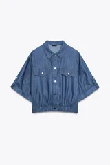 Cazadora de denim azul con mezcla de algodón y lino. Tiene cuello solapa, manga corta con vuelta y trabilla con botón, bolsillos de plastrón en el delantero, bajo elástico y cierre frontal con botones.