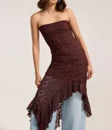 Vestido blanco sin breteles, confeccionado en encaje floral. Presenta un escote recto y un bajo asimétrico con volados.