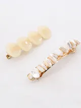 Set de dos hebillas para el pelo, una con cuatro cuentas redondas color crema y otra con incrustaciones de piedras irregulares color crema.