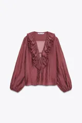 Blusa color ladrillo confeccionada en hilatura con mezcla de lyocell, escote pico ajustable con cordones, manga larga con volumen acabada en elástico y detalle de volantes en el mismo tejido.