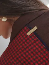 Blazer oversize con diseño asimétrico que combina dos tweeds contrastantes: uno marrón liso y otro blanco y negro con estampado pata de gallo. Tiene botones de strass y un pin de salchicha.