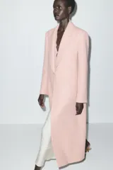 Abrigo largo color rosa pálido, de corte recto, con cuello solapa, cierre frontal con un botón y bolsillos laterales de ojal.