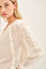 Camisa de manga larga color crudo, confeccionada en viscosa plumeti. Posee cuello redondo con tajo delantero y volados verticales.