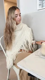 Ruana color crema tejida a mano con lana merino, con cuello alto y flecos.