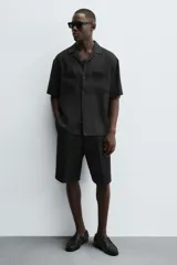 Zapato náutico de vestir color negro, con parte superior lisa, bordón, detalle de ojales metálicos, horma redonda y suela a tono con ligero tacón.