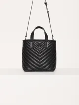 Cartera tote pequeña de cuero sintético negro con diseño acolchado en forma de espiga. Tiene doble asa corta superior, correa larga ajustable y desmontable, y logo metálico frontal con forma de labios.