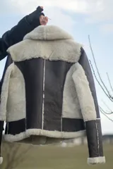 Campera gamulán marrón con interior de piel sintética blanca, cierre frontal con cremallera, cuello con solapas y dos bolsillos con cierre.