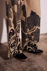 Pantalón de lino color beige con estampado de hojas negras, corte flare y tiro alto.