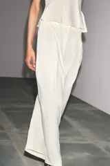 Pantalón culotte color crudo, de tiro medio, confeccionado en lino. Presenta bolsillos laterales, pinzas delanteras, pierna ancha y cierre frontal con cremallera, botón y ganchos metálicos.