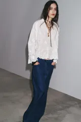 Blusa blanca de algodón con cuello solapa, escote pico y manga larga acampanada. Detalle de frunces y bordados a tono.