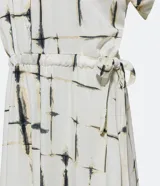 Vestido midi de viscosa color blanco con estampado de bloques negros, corte evasé, mangas cortas, cuello camisero, lazo en la cintura y cierre frontal con botones.