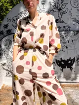 Camisa de manga corta con estampado de lunares marrones, amarillos y rosados sobre fondo blanco. Tiene cuello camisero y cierre con botones.